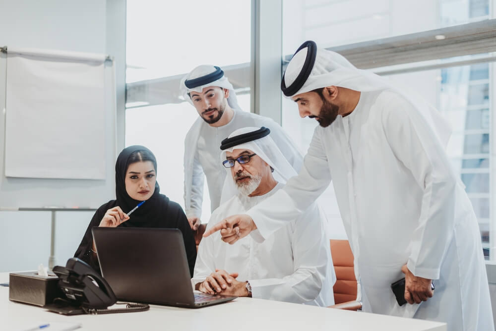 three saudi arabia men and a single woman discussing finances ona alptop