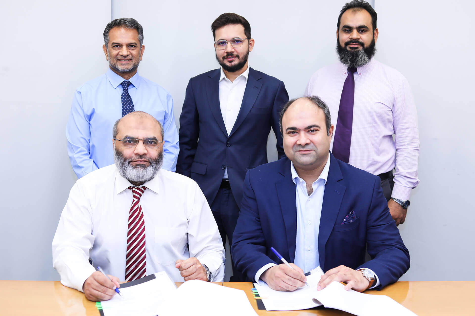 The foreground features two seated men, each holding a pen and presumably signing documents related to the collaboration. These key figures include Ibrahim Ahmed Zahidie, Prima Consulting’s Director of Financial and Accounting Advisory, and Muhammed Aasim Gul, Chief Financial Officer. Behind them stand four more individuals, including Baber Mahmood Mirza, Atlas Insurance’s Chief Executive Officer, and Omer Yousuf, Atlas Insurance’s Vice President. Additionally, Sumar Sayani, Prima Consulting’s Director of AI and Tech, completes the group. The backdrop prominently displays the Delta logo, symbolizing the strategic partnership between Atlas Insurance and Prima Consulting. This landmark deal aims to seamlessly embrace IFRS 17 regulations using Prima Consulting’s innovative Delta IFRS 17 software, tailored specifically for the insurance industry.