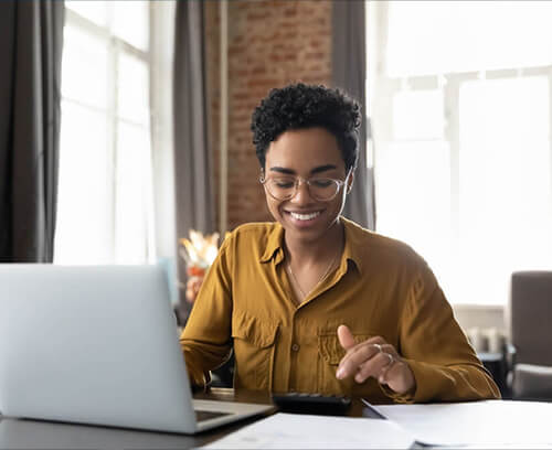 An individual in a professional office setting, focused on a laptop and holding a calculator