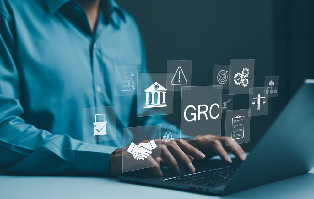 Person typing on a laptop with floating icons representing GRC (Governance, Risk, and Compliance) services.