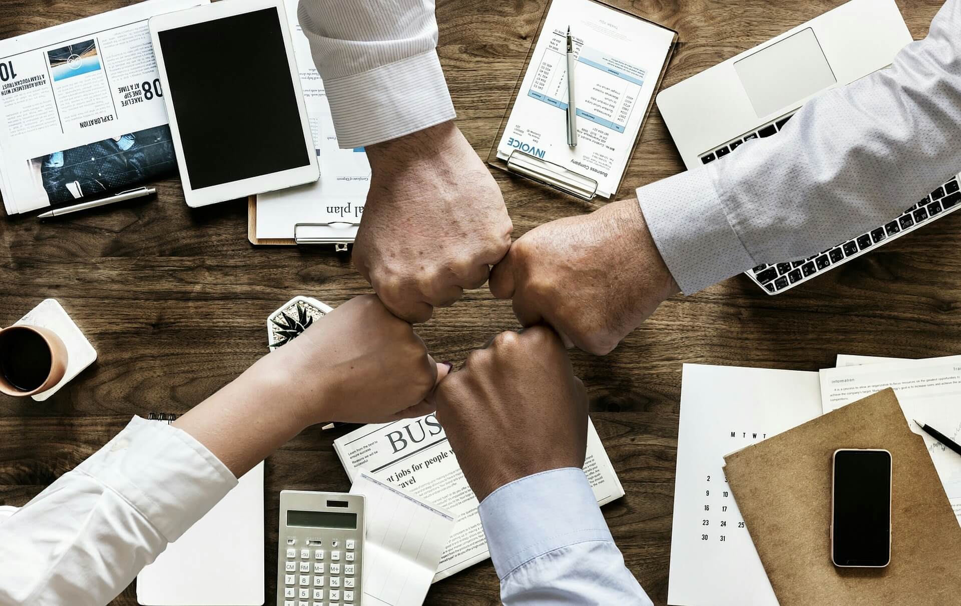 A group of hands coming together, symbolizing teamwork and integration in a business setting. The hands are giving fist bump, suggesting the seamless merging of companies or systems as referenced by IFRS 3 Business Combination.