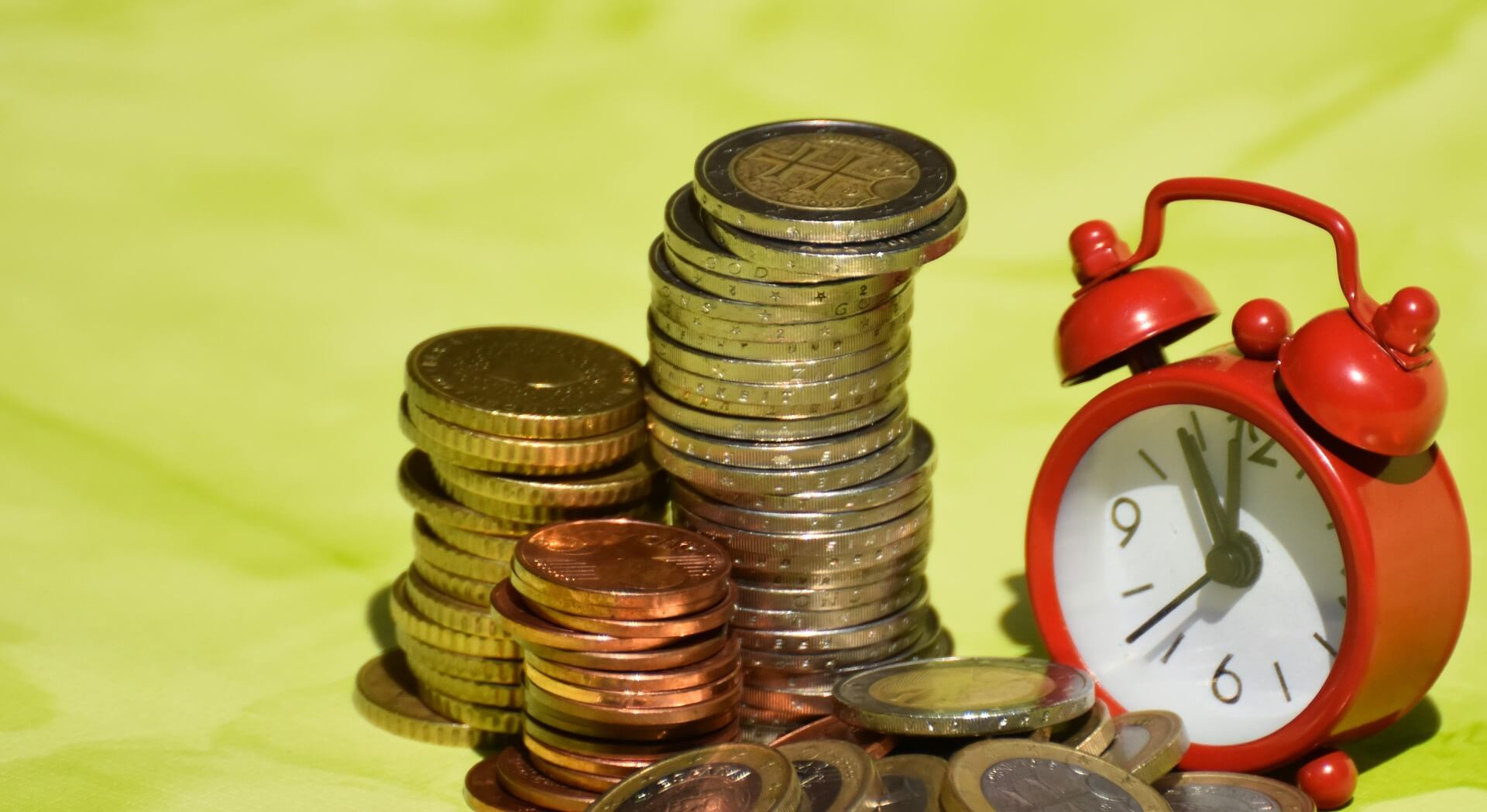 Stacked coins beside a red alarm clock, symbolizing the importance of time and accuracy in Technical Reserves Valuation.