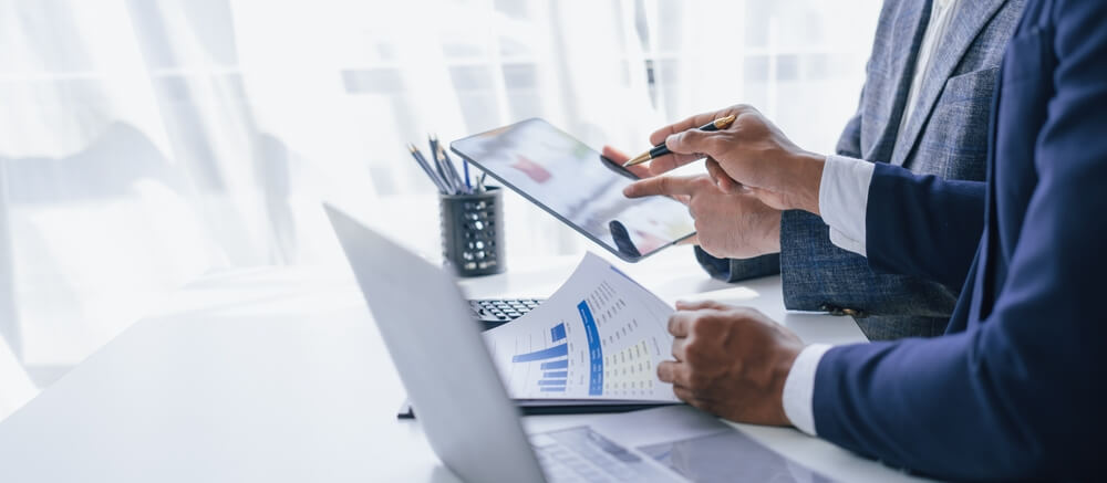 Two professionals discussing data on a tablet and paper charts during an Internal Audit Consulting session.