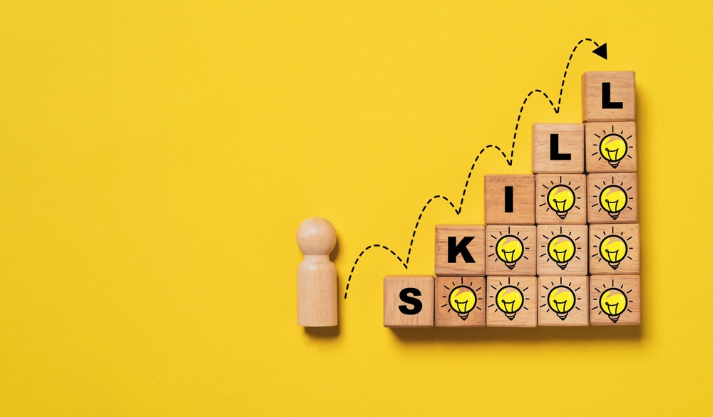 Wooden figure and blocks spelling "SKILL" with lightbulb icons, symbolizing growth through Training Programs.