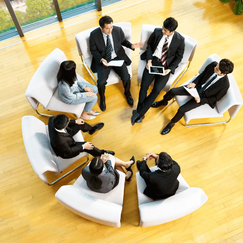 A group of professionals in business attire sit in a business circle, engaged in a strategic discussion.