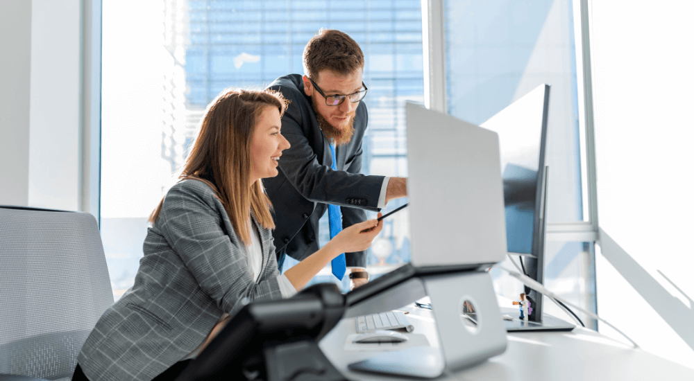 Two colleagues discussing financial data on a computer, highlighting the importance of ARK9 EIR IFRS compliance software for accurate reporting.