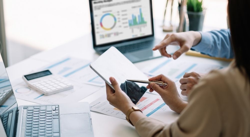 Two professionals reviewing financial documents and a laptop displaying charts, representing ARK9 EIR Financial Reporting Software's dashboards.