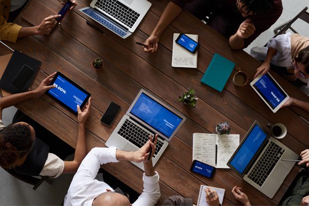 A top-down view of a team meeting around a wooden table, reviewing IFRS 16 data on tablets and laptops, with notebooks and coffee cups present.