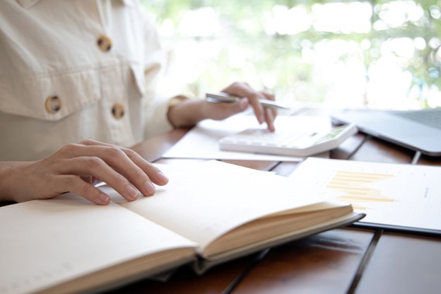 A person working with a calculator and notebook, analyzing IFRS 15 revenue from contracts with customers data in a bright office setting.