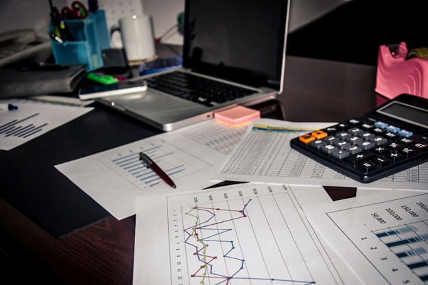 A cluttered office desk with charts, a calculator, and a laptop, illustrating the analytical work involved in IFRS 17 financial reporting.