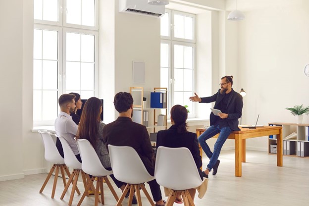 A presenter addressing a group in a meeting room, discussing employee benefits valuation using a tablet.