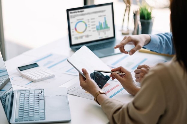 Professionals reviewing IFRS 16 advisory documents on a laptop with charts and graphs, holding a tablet and paper reports in a collaborative office setting.