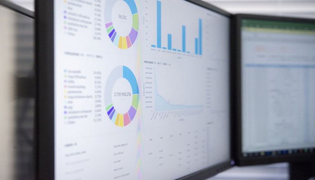 A computer screen displaying actuarial valuation services data with colorful pie charts and bar graphs, showing detailed financial analysis in a professional office setting.