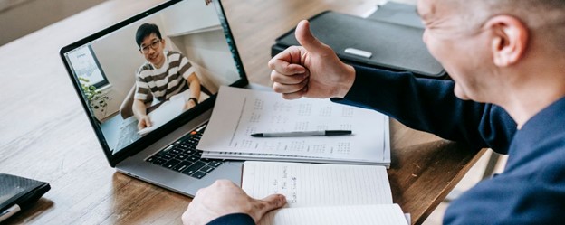 A person giving a thumbs-up during a virtual meeting focused on employee benefits valuation, with notes and a laptop on the table.