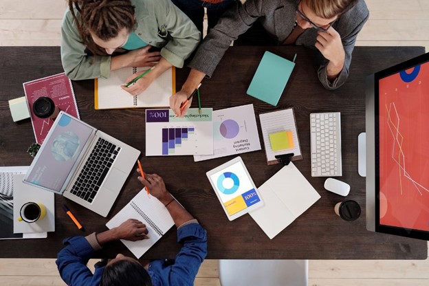 A team collaborating on actuarial valuation services, working with laptops, charts, and documents on a wooden table in a creative office environment.