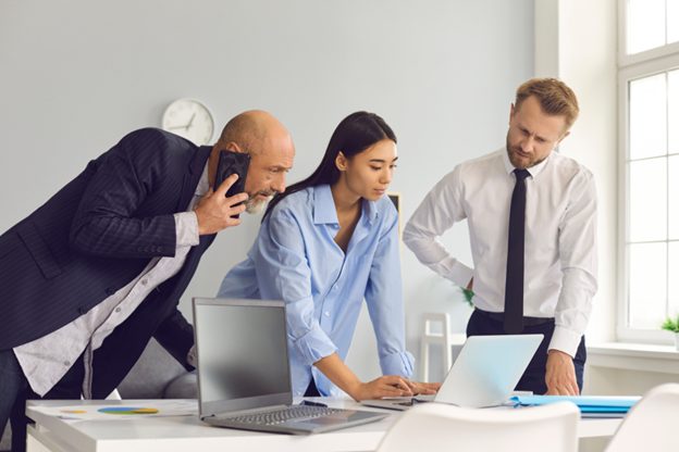 A professional office setting with three colleagues collaborating around a table, using laptops and a phone, discussing IFRS 16 financial data on the screen.